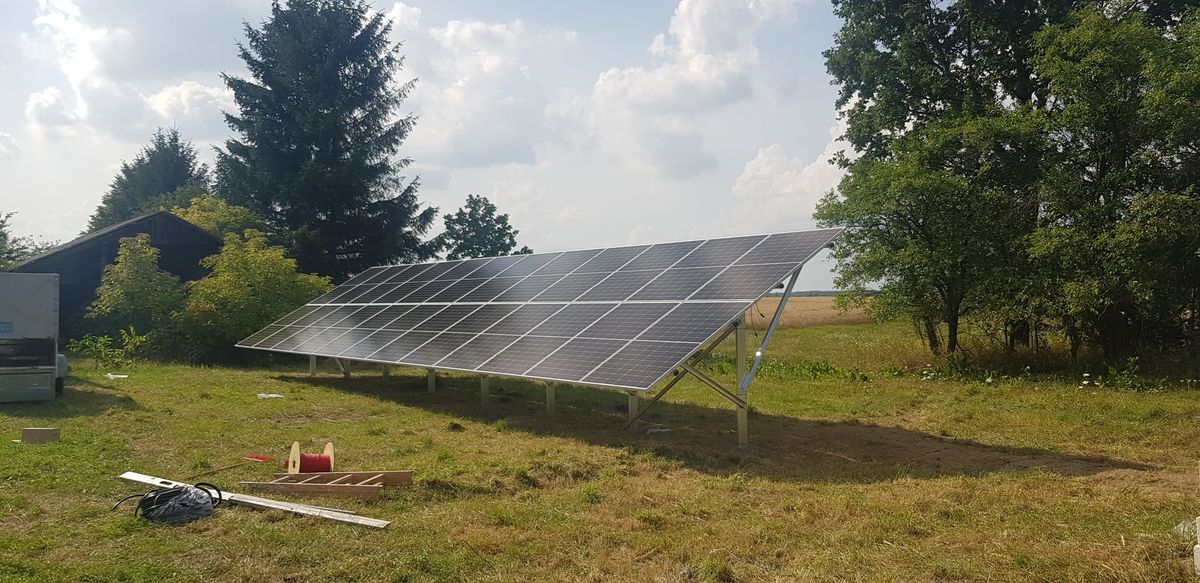 Naziemna instalacja fotowoltaiczna ustawiona na trawniku obok zabudowań